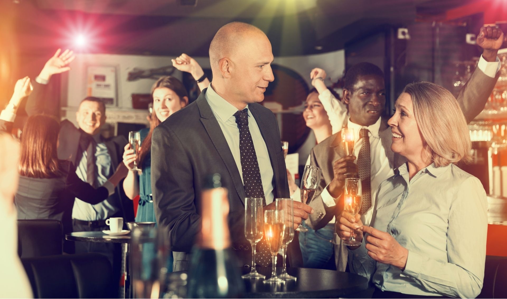 A group of people in business attire are socializing and celebrating with drinks at an indoor event or party.