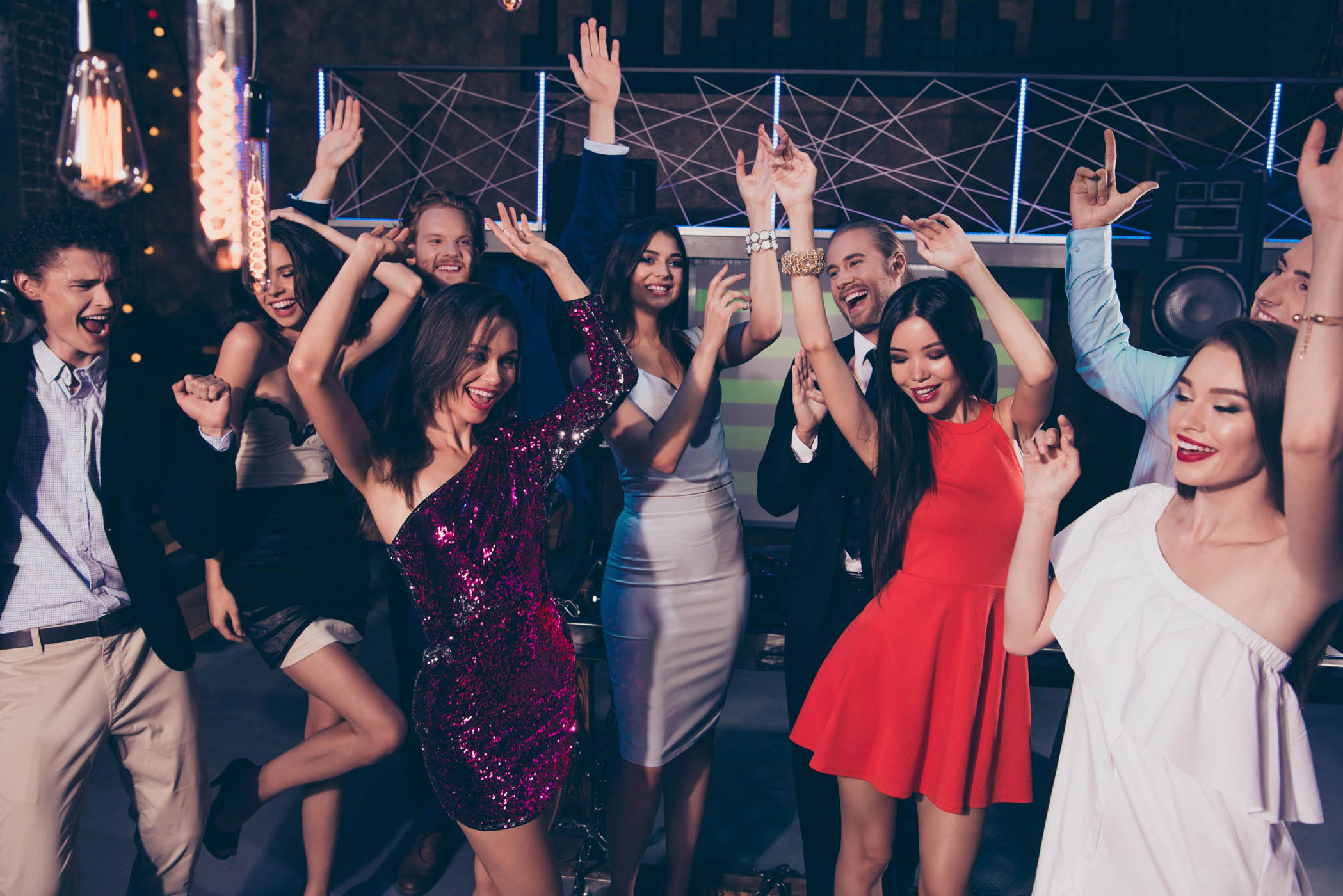 A group of people dressed in semi-formal attire are dancing and smiling at an indoor corporate event with colorful lighting and premium events add ons features enhancing the experience.
