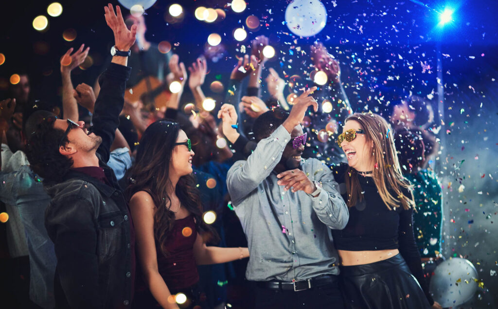A group of people dancing and celebrating at a corporate event with confetti falling and colorful lights in the background.