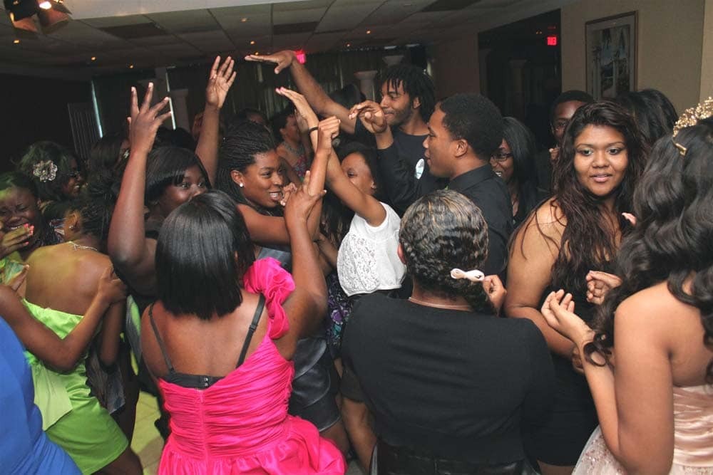 A group of young people dressed in formal attire dance and celebrate together at an indoor event.