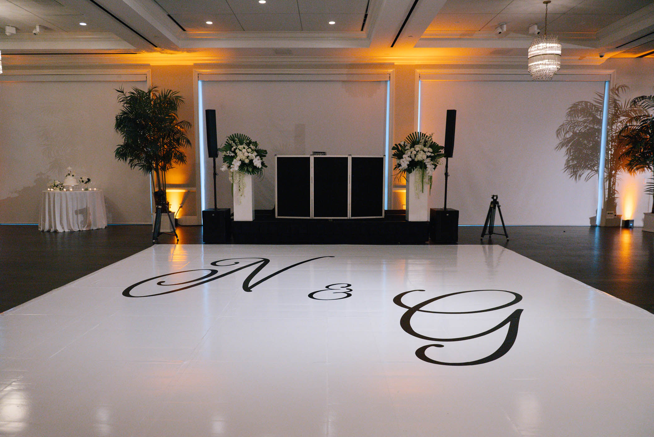 A decorated event space with a white L.E.D. Dance Floor featuring large black letters "N & G," a DJ booth, speakers, and floral arrangements.