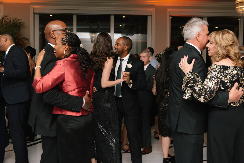 Guests in formal attire dance and mingle at an indoor event, capturing the vibrant atmosphere you can expect when you contact Edifying Beats.