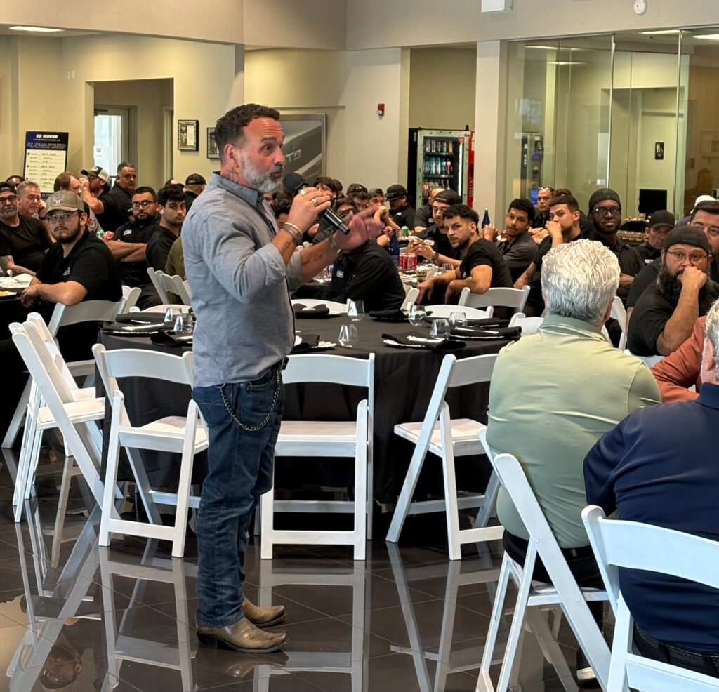 A man speaks into a microphone to a seated audience in a conference room with black tablecloths and white chairs, setting the tone for memorable corporate events.