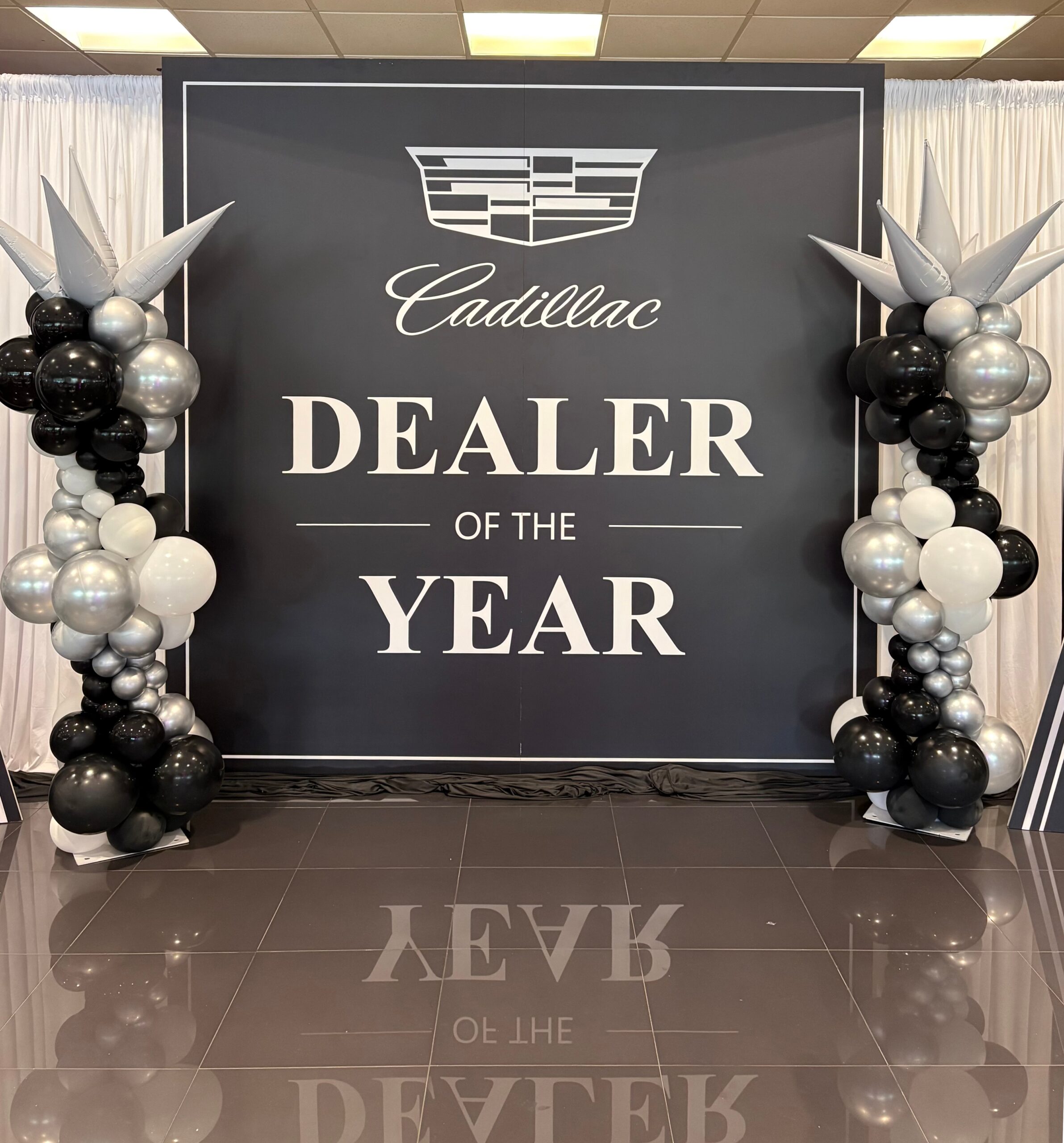 Cadillac Dealer of the Year backdrop with black, white, and silver balloon arrangements on each side, displayed on a shiny floor with white curtains behind—creating a sophisticated gallery atmosphere perfect for capturing memorable moments.